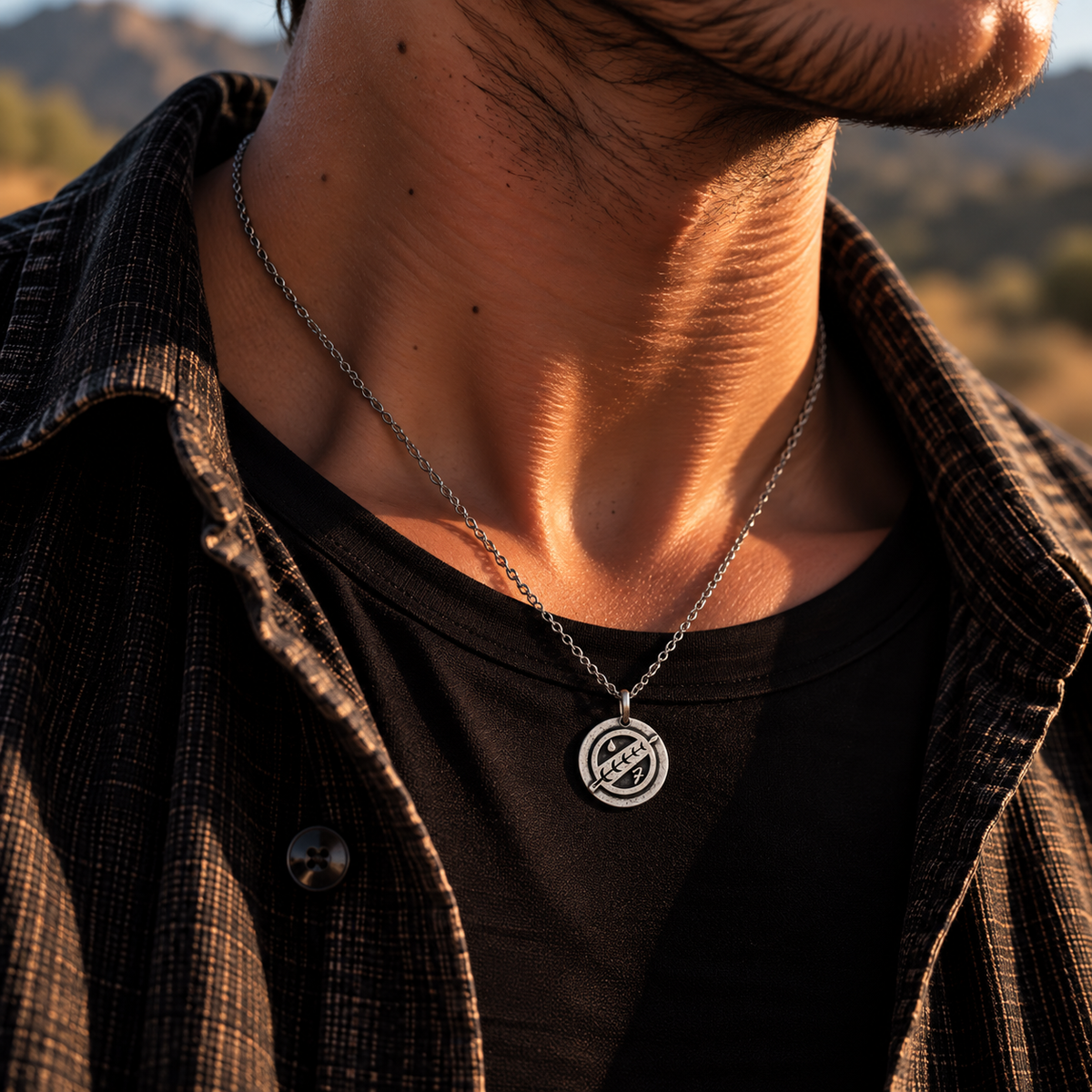 Silver-tone Boba Fett crest necklace worn over a black shirt at sunset.