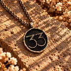 Gold-tone Expedition 33 medallion necklace with raised 33 numerals on a dark background on stone.