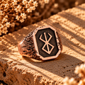 Rose gold rune signet ring with dark inlay and raised runic symbol.