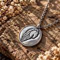 Silver-tone Riders of Rohan horse crest medallion necklace with a flowing mane motif on stone beside dried flowers.
